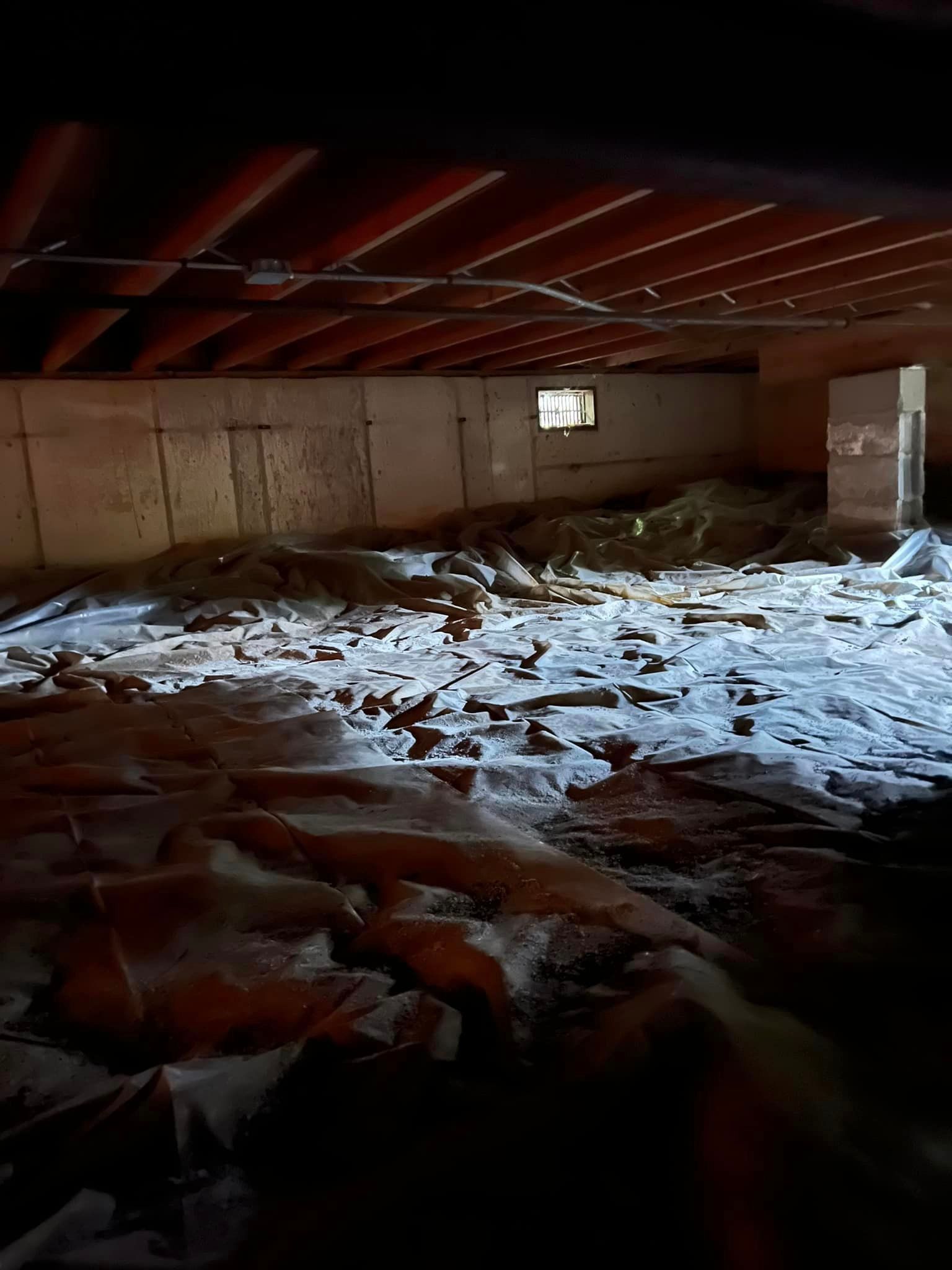 A dark room with a lot of trash on the floor and a window.