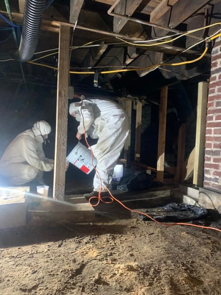 Two men in protective suits are working in a basement.