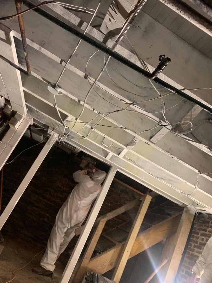A man in a white suit is working on a ceiling in a basement.