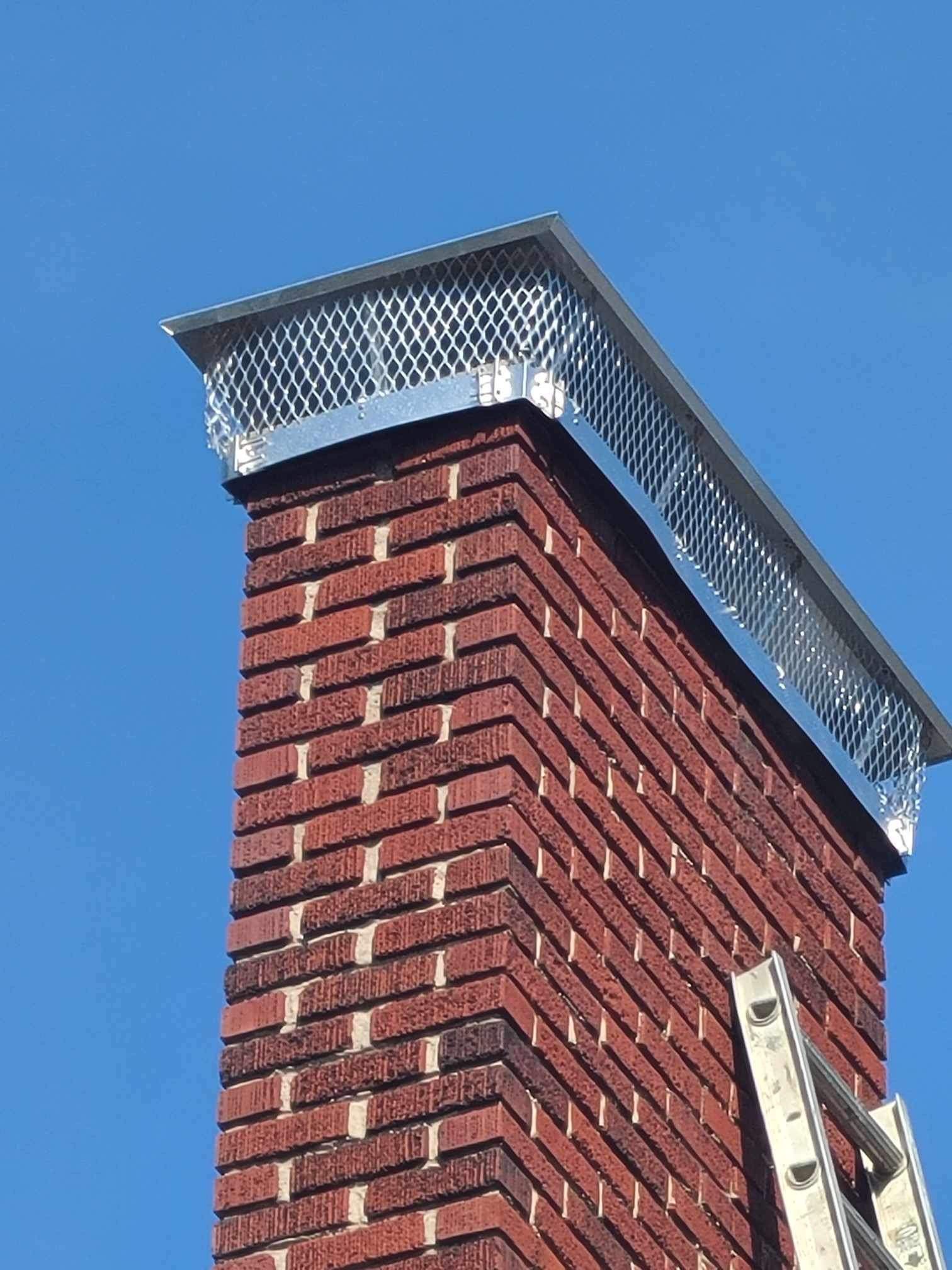 A brick chimney with a ladder attached to it against a blue sky.