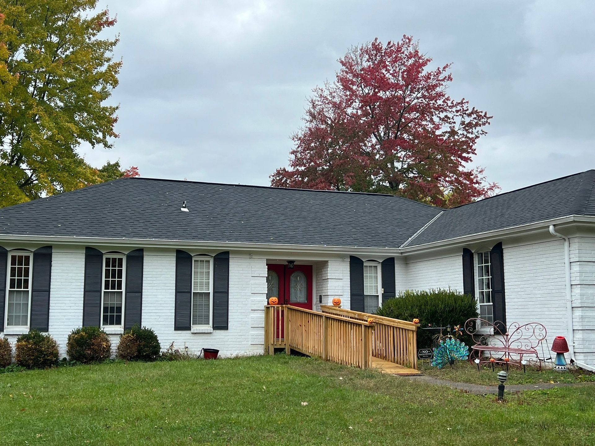 A white house with black shutters and a wooden ramp in front of it.