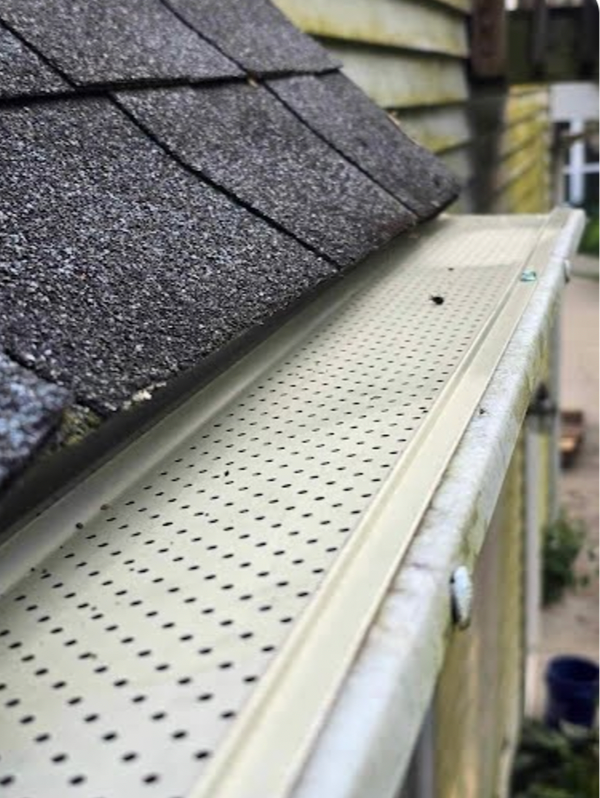 A gutter on the side of a house with a roof in the background.