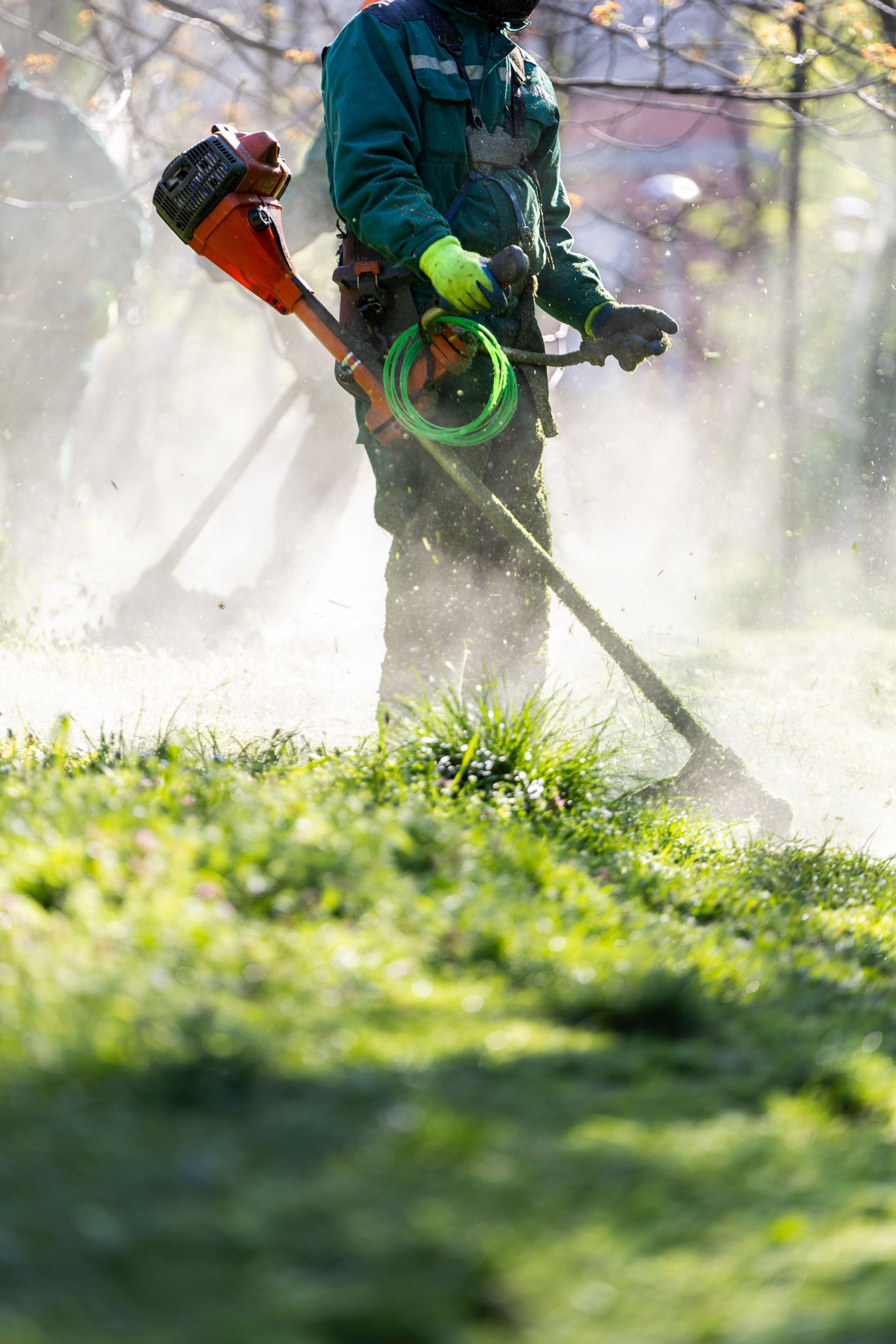 Worker using a leaf blower to clear grass, with dust and debris spraying in a yard