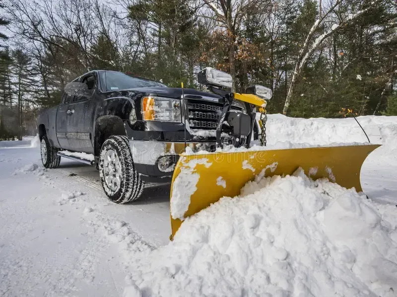 Black pickup with yellow snowplow clearing snow on a snowy road in winter