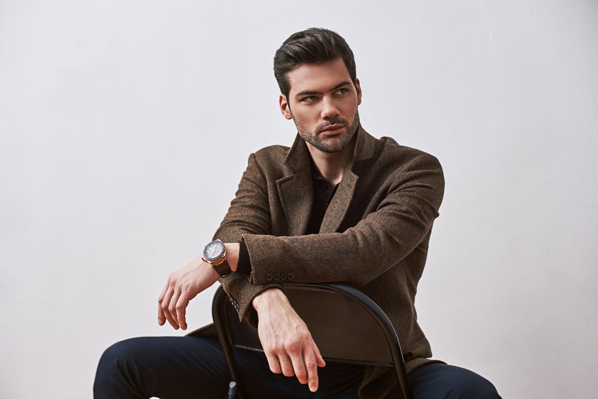 Perfect style. Stylish dark-haired man sitting on a chair and looking away