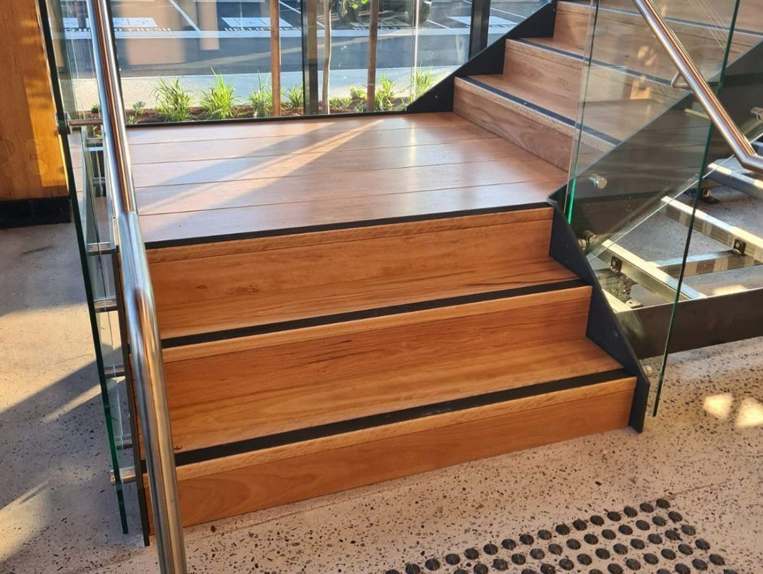 Wooden staircase with glass railings, black non-slip strips. Indoors — Zeal Interiors in South Grafton, NSW