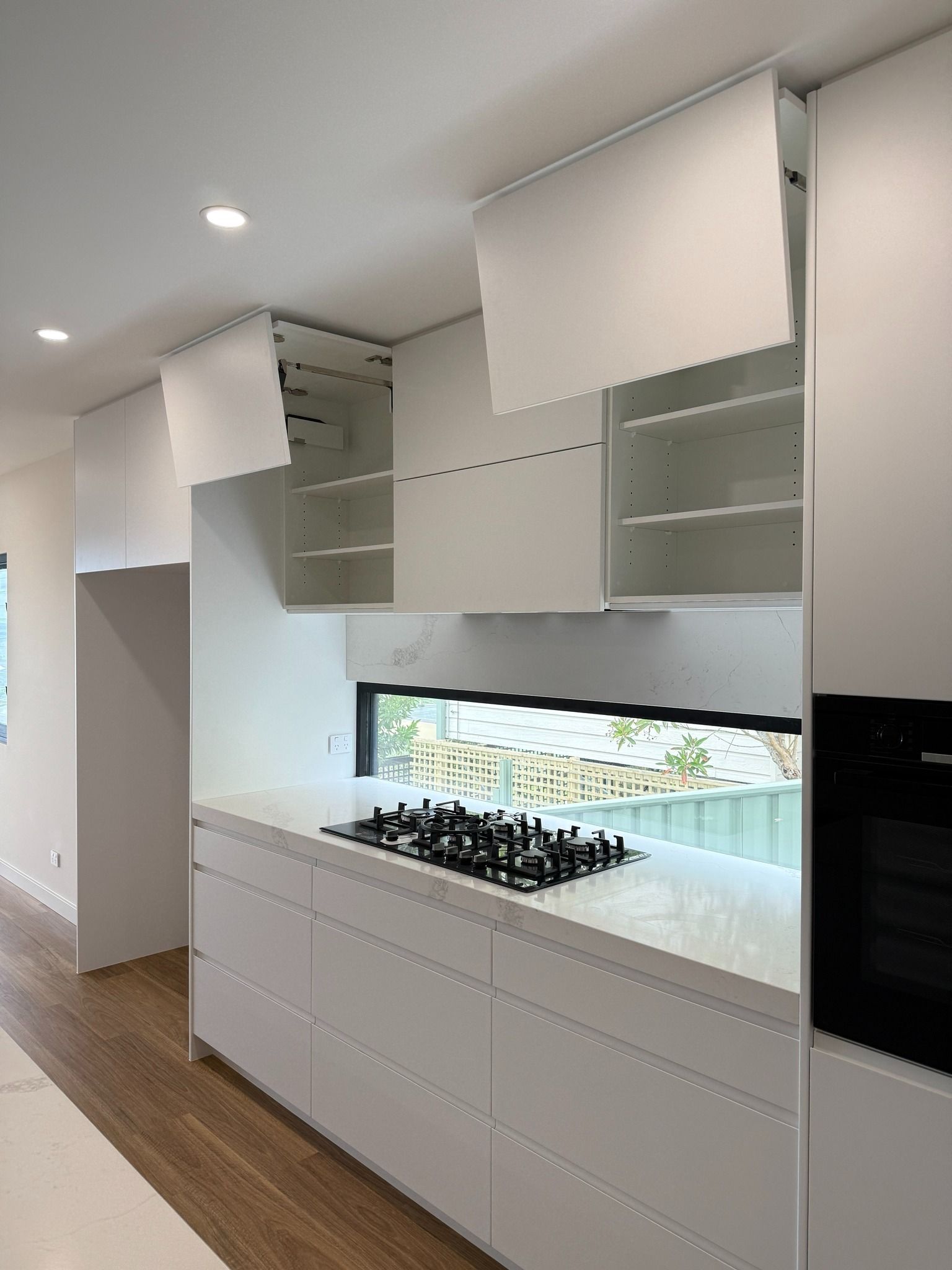 Modern White Kitchen With Overhead Cabinets Open, Stove Top, and Oven — Zeal Interiors in Brisbane, NSW