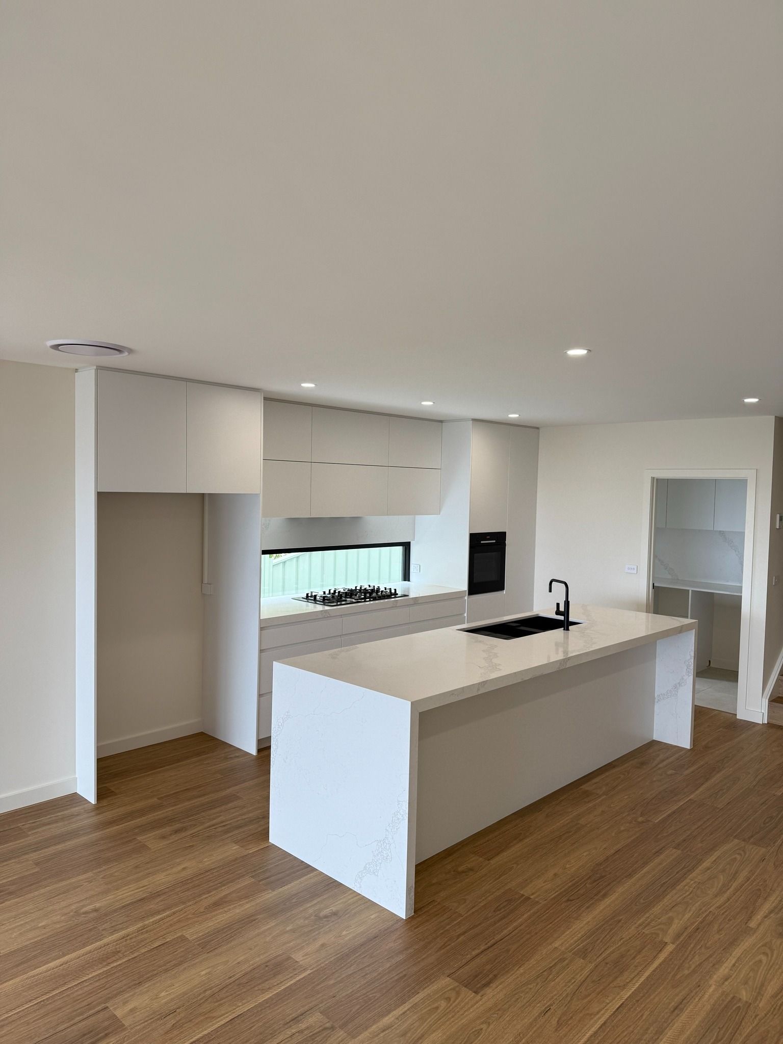 Modern White Kitchen With Island, Wooden Floors, and Built-in Appliances — Zeal Interiors in Eastern Creek, NSW