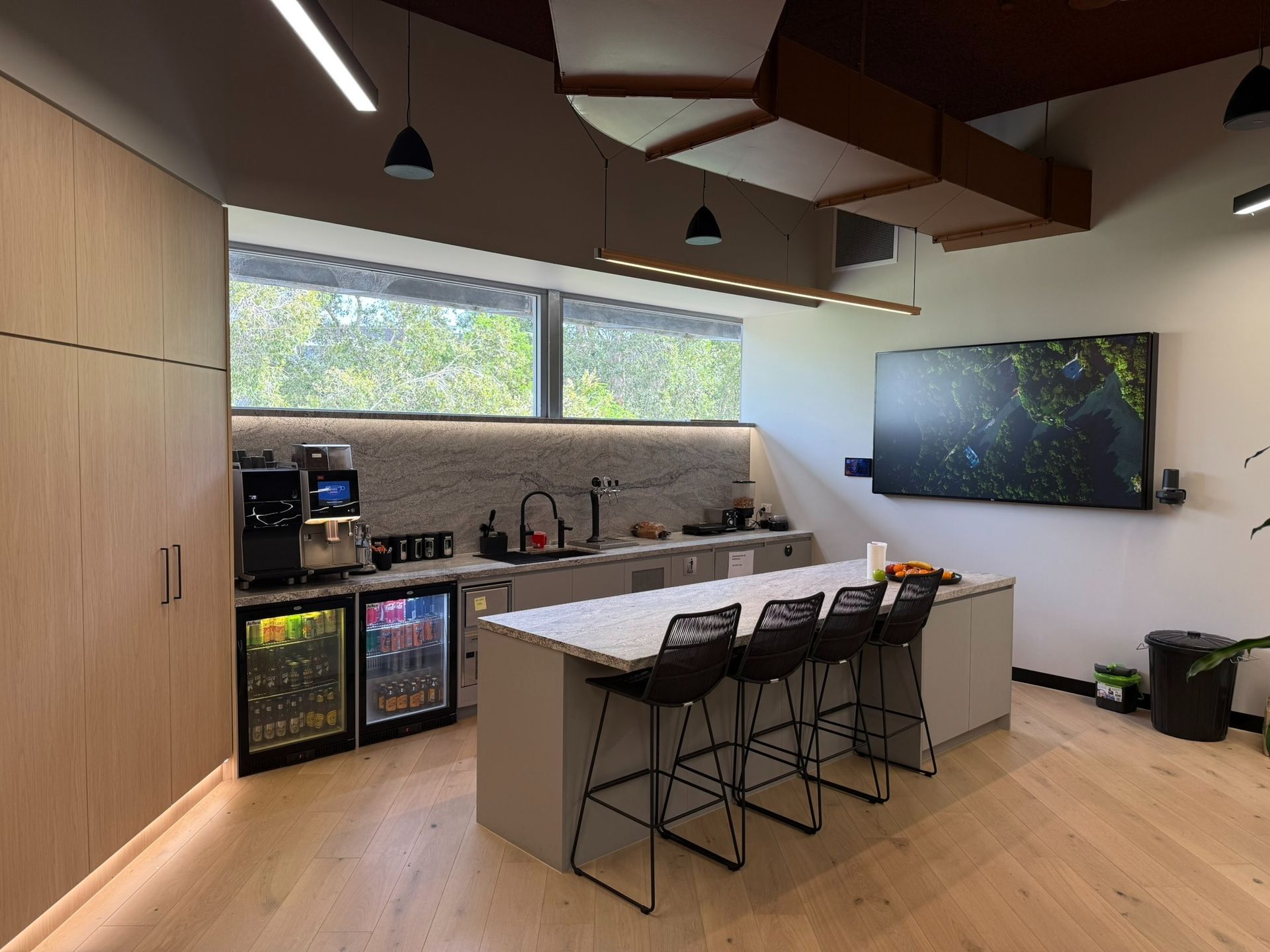 Modern Office Breakroom With a Kitchen Island, Stools, Cabinetry, and a Large Tv — Zeal Interiors in Brisbane, NSW