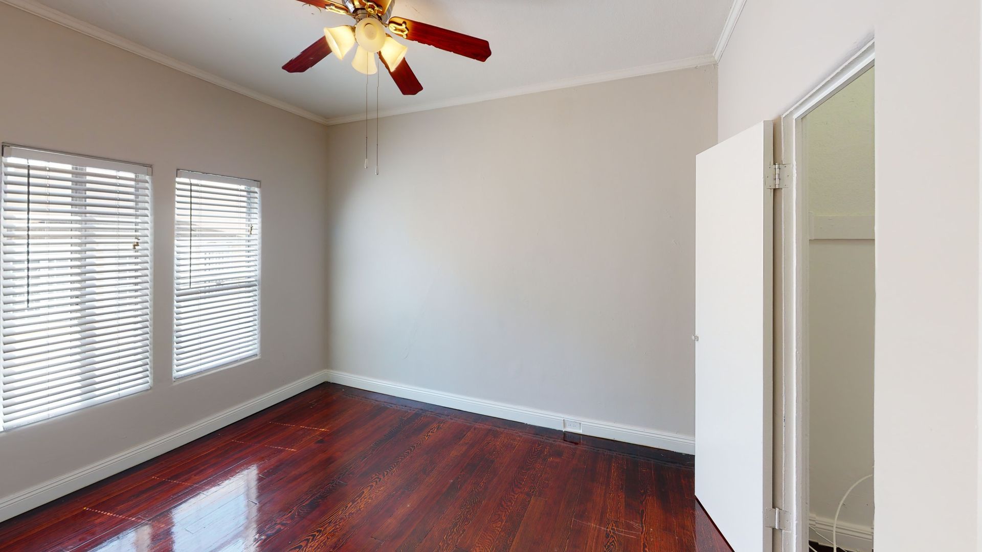 Empty bedroom with hardwood floors, two windows with blinds, and a ceiling fan.