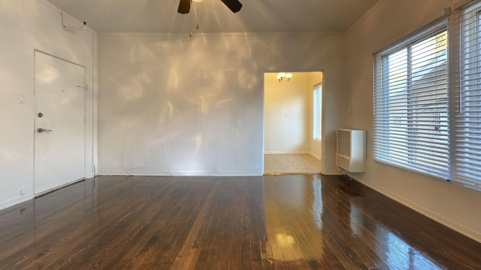 Empty room with dark wood floors, white walls, and a window with blinds.