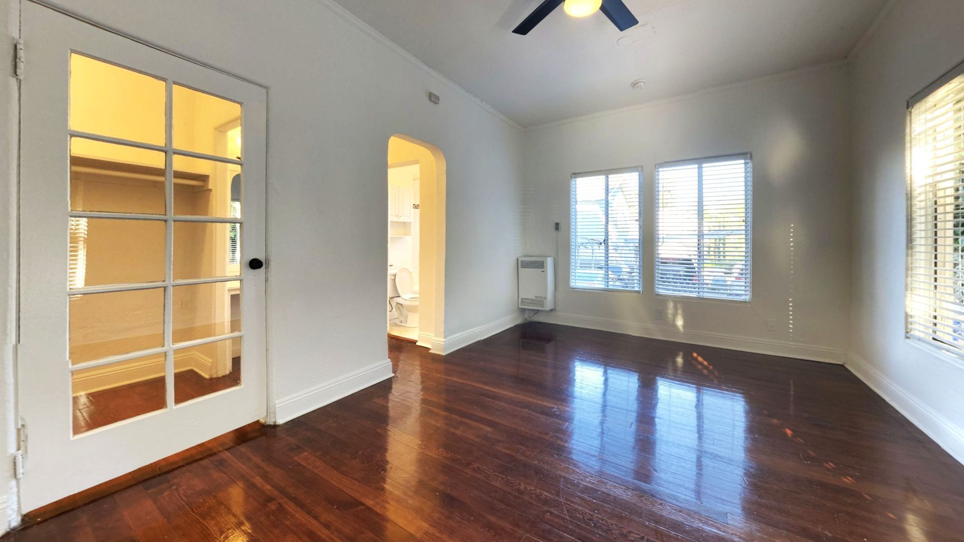 Empty room with hardwood floors, windows, closet door, and an arched doorway.