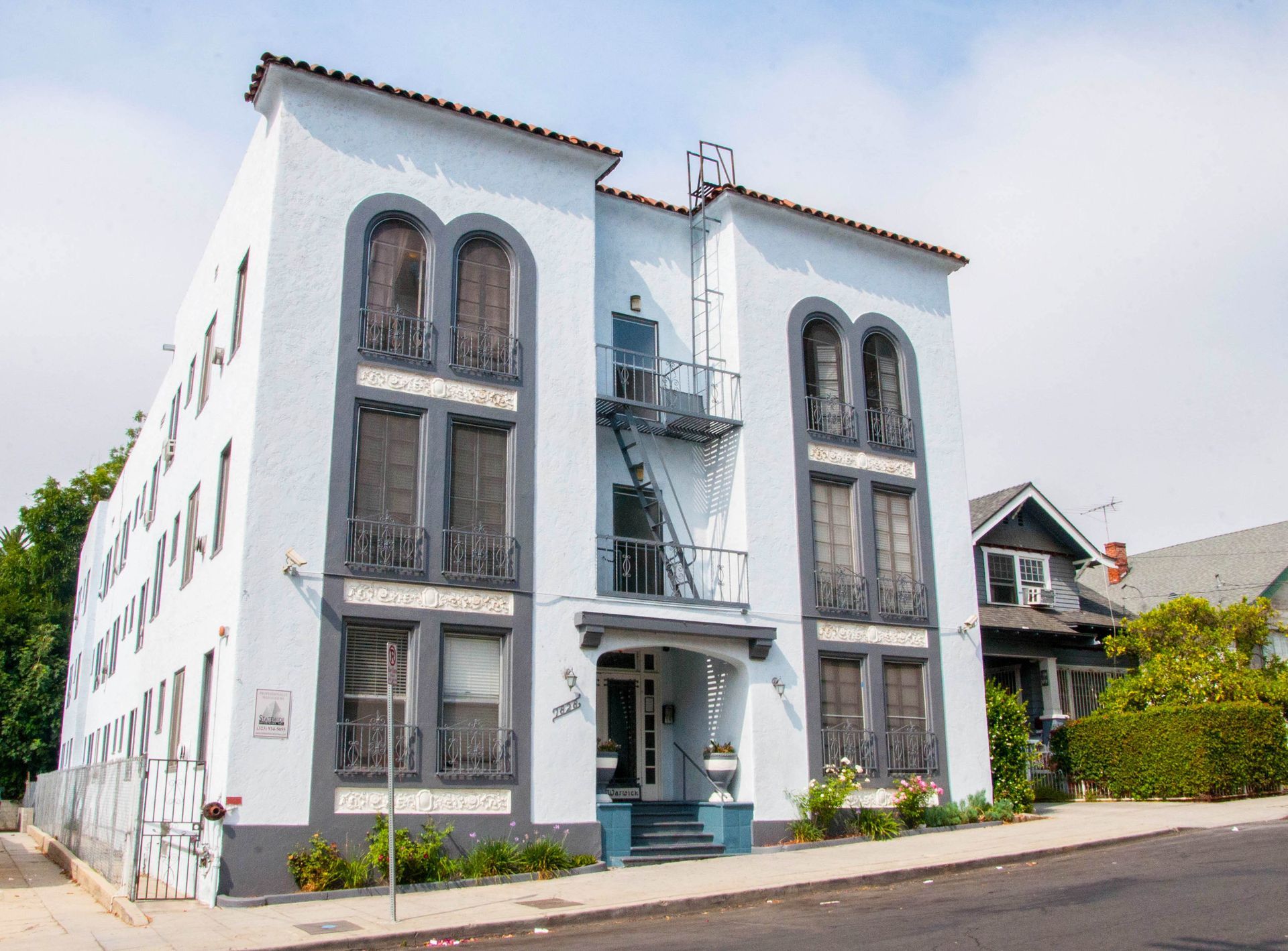 Three-story light blue apartment building with gray trim. A fire escape runs up the middle.