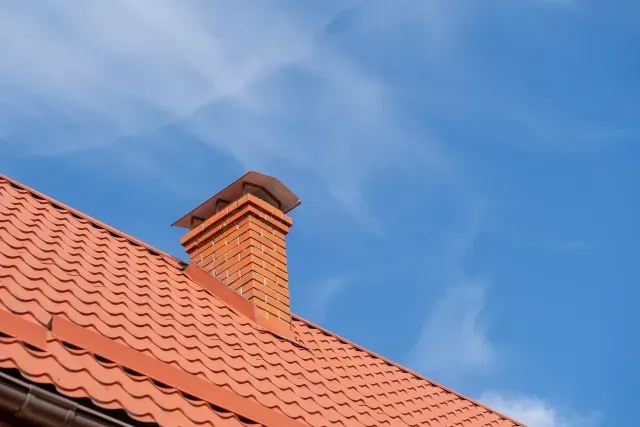 Chimney Sweep Portland Maine - Red-tiled roof with a brick chimney against a clear blue sky, showcasing a serene architectural detail.