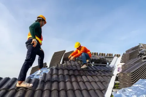 Chimney sweep portland maine - Two workers in hard hats and safety gear are repairing a tiled roof under a clear blue sky.