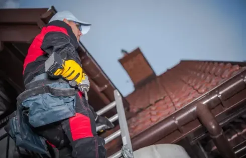 Chimney sweep portland maine - A worker in a red and black uniform climbs a ladder to a roof, holding a drill and wearing gloves, ready for repairs.
