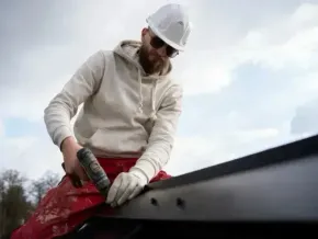 Chimney sweep portland maine - Construction worker in hard hat and gloves applies sealant to roof.