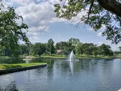 Chimney sweep portland maine- A serene lake with a fountain is surrounded by lush green trees under a partly cloudy sky.