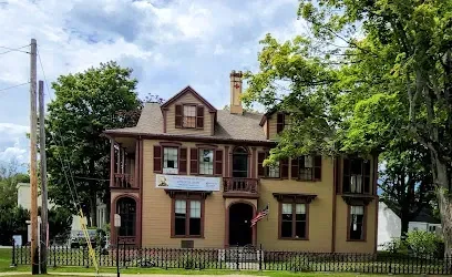 Chimney sweep portland maine-A tan Victorian house with dark red trim, balconies, and an American flag stands on a tree-lined street under a cloudy sky.