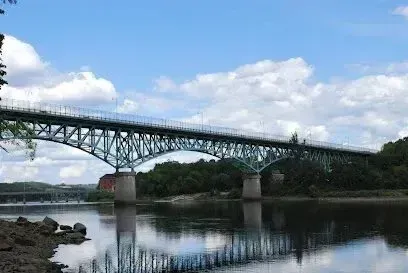 Chimney sweep portland maine -Green truss bridge spanning a wide river under a partly cloudy blue sky.