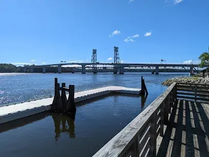 Chimney sweep portland maine-A modern drawbridge spans a wide river with a floating dock in the foreground under a clear blue sky.