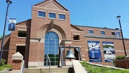 Chimney sweep portland maine-Brick building with a large arched window, a bell, and informational banners under a clear blue sky.