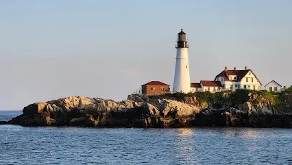 Chimney sweep portland maine- A white lighthouse with a black top stands tall on a rocky island with several connected buildings.