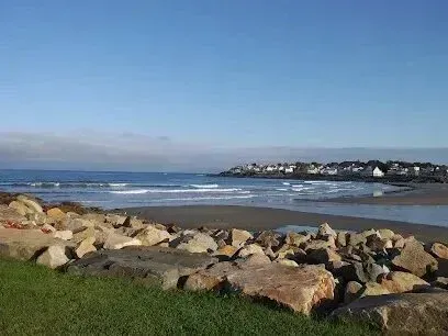 Chimney sweep portland maine-Rocky shoreline with a calm ocean and distant coastal town under a clear blue sky.