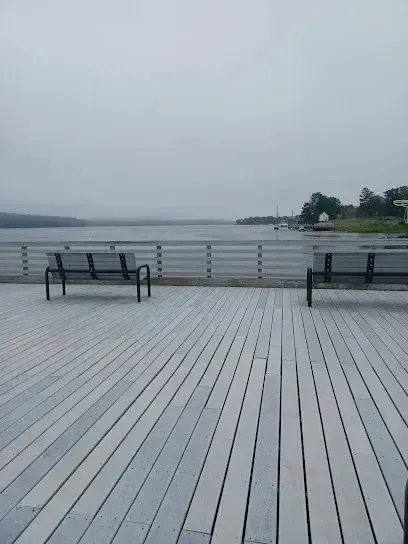 Chimney sweep portland maine- Two empty park benches sit on a wooden boardwalk overlooking a calm body of water under a cloudy sky.