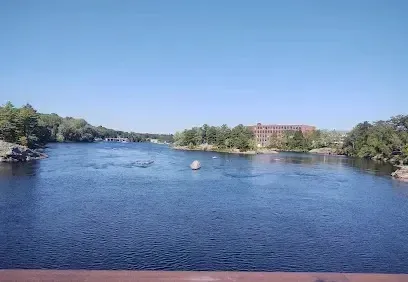 Chimney sweep portland maine - Wide river flows past tree-lined banks toward a large brick building under a clear blue sky.