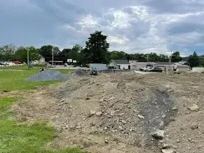 Chimney sweep portland maine - Construction site with piles of gravel, heavy machinery, and buildings under a cloudy sky.