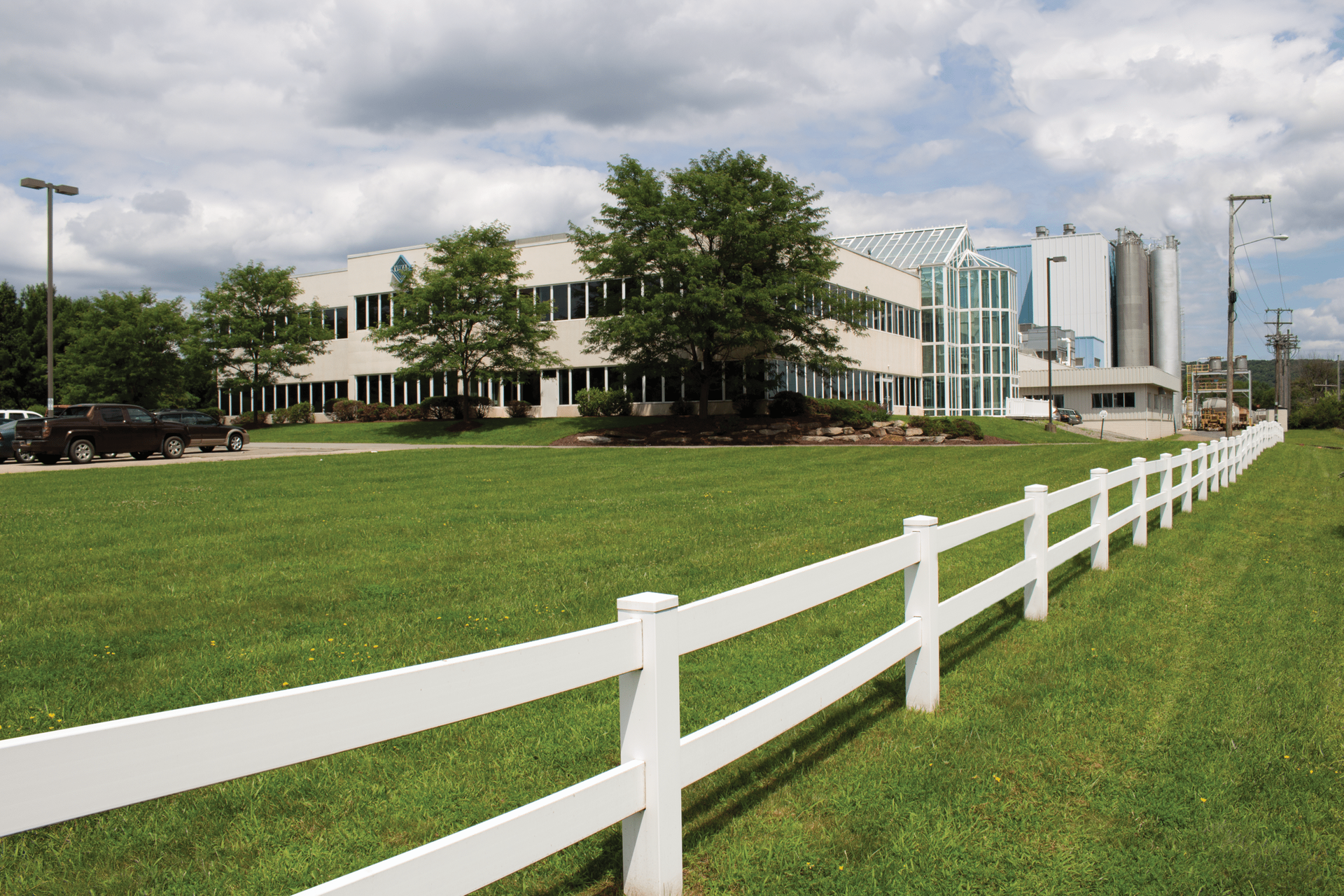 A white fence surrounds a grassy field in front of a building