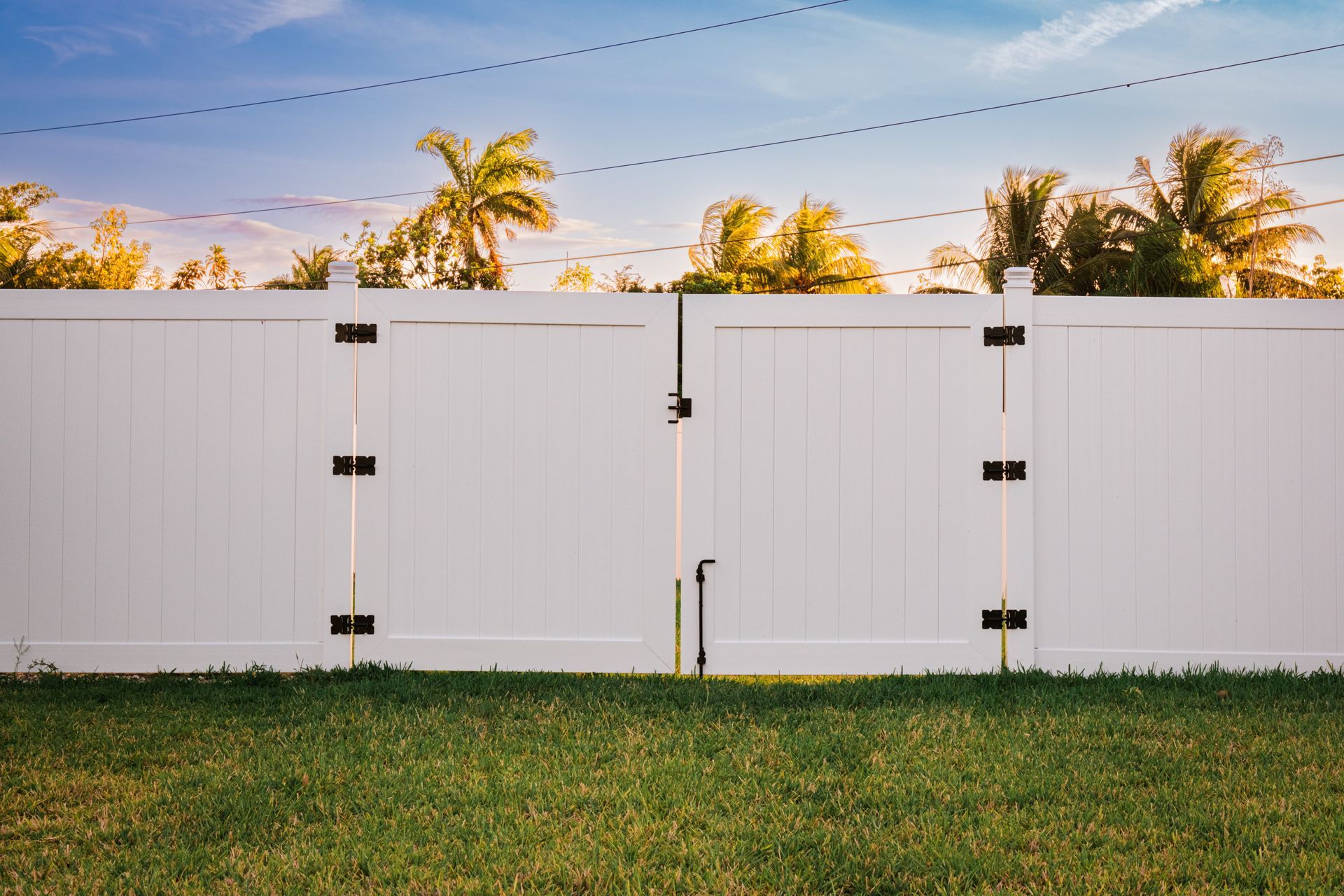 A white fence with a gate in the middle of a lush green field.