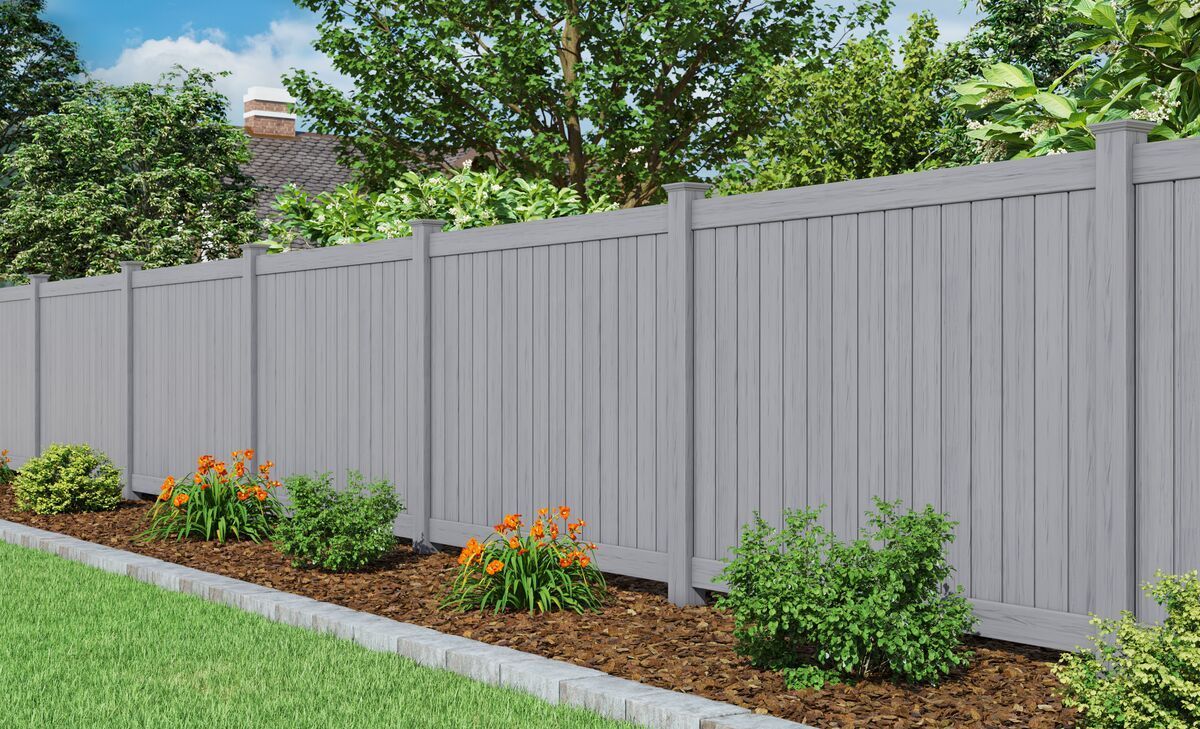 A gray fence surrounds a lush green yard with flowers and bushes.