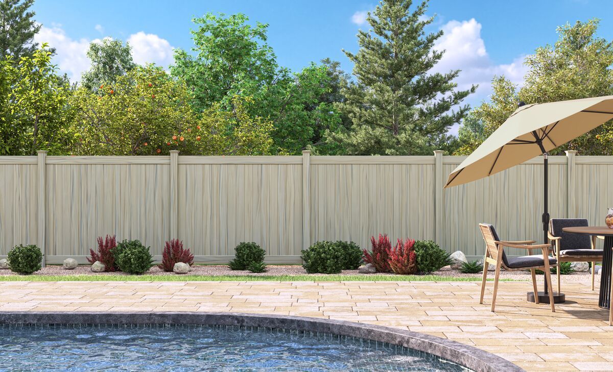 A fence surrounds a swimming pool with a table and chairs and an umbrella.