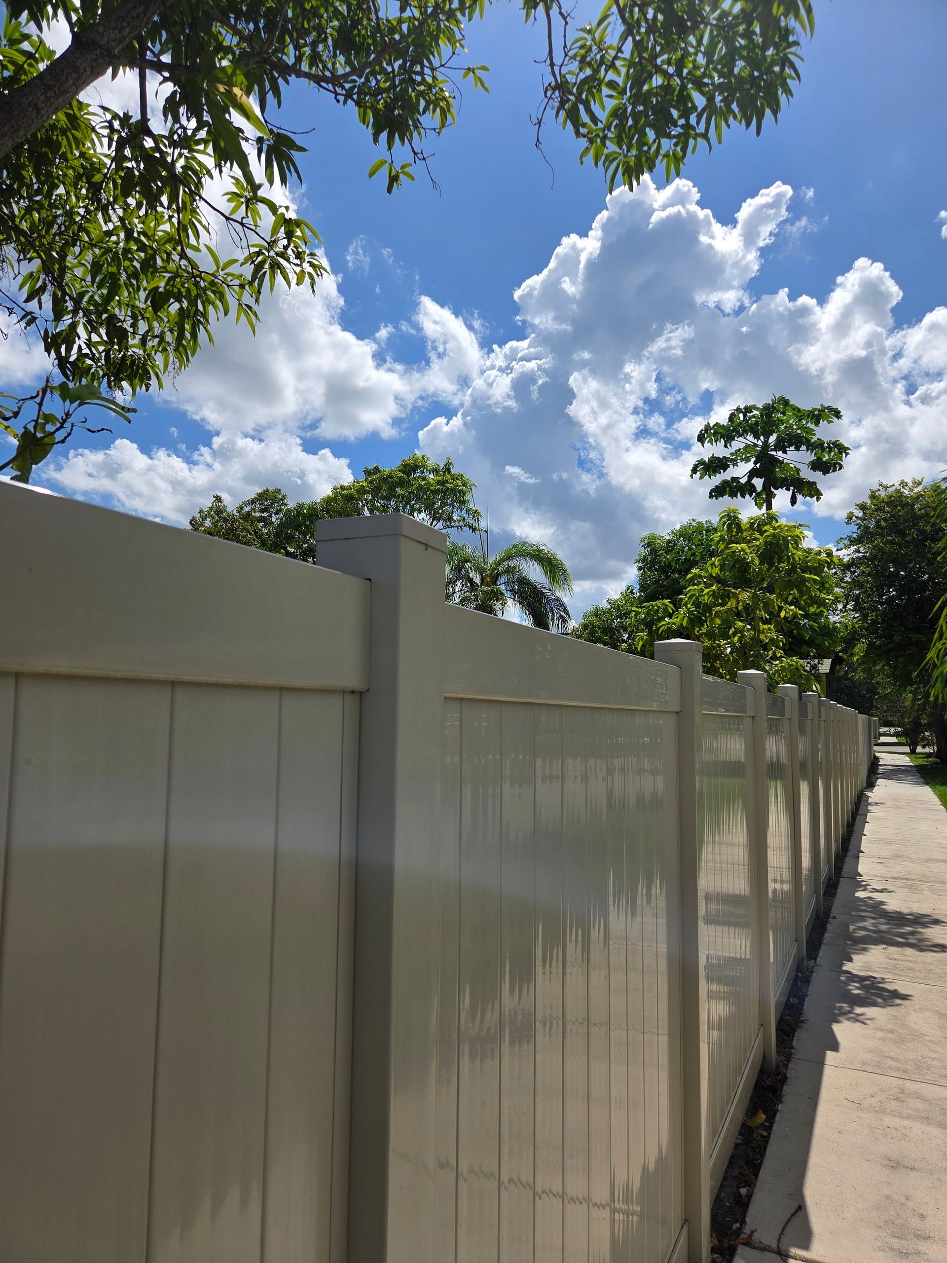 Beige vinyl fence on a sunny day with blue sky and trees.