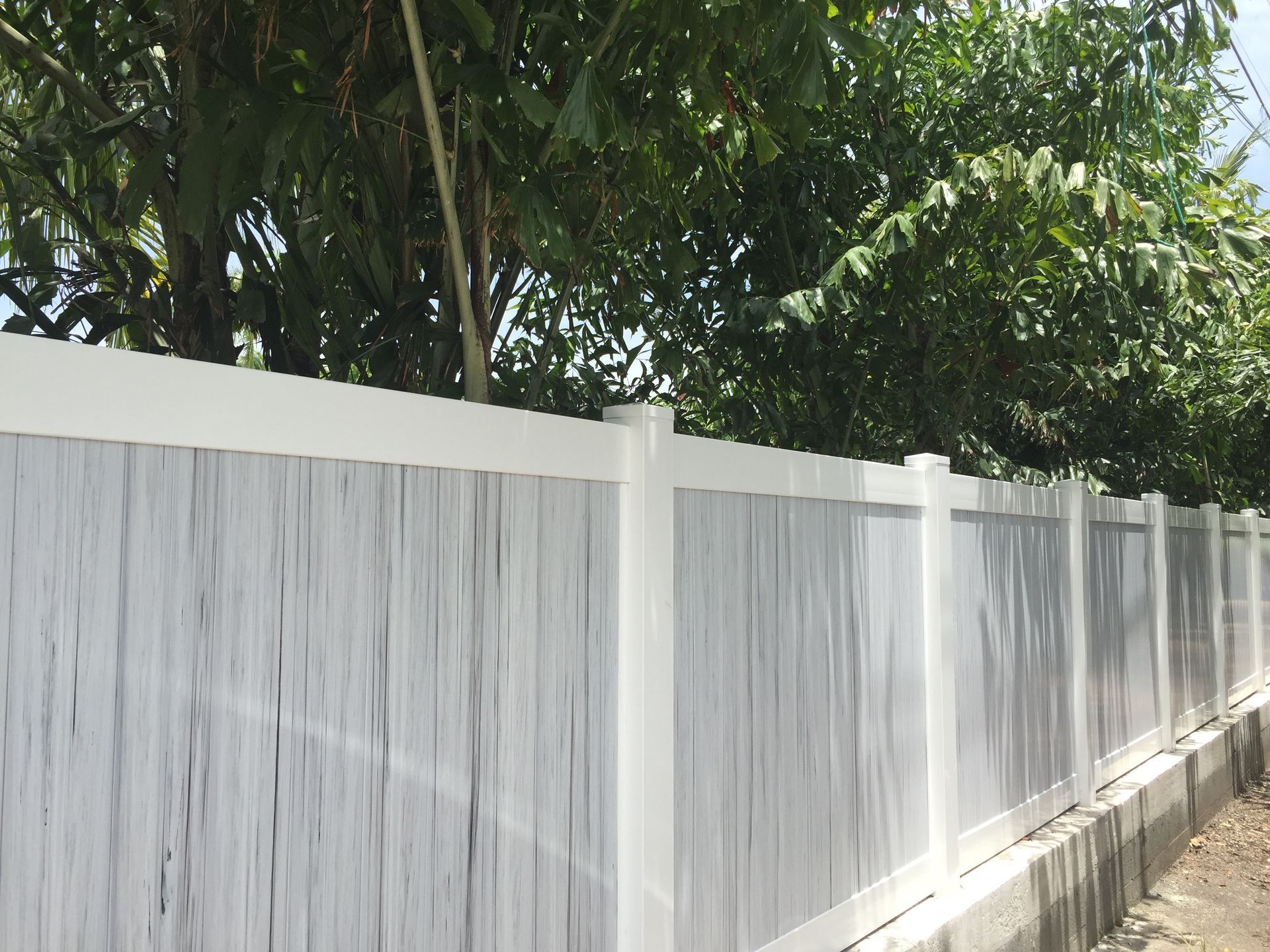A white wooden fence with trees in the background