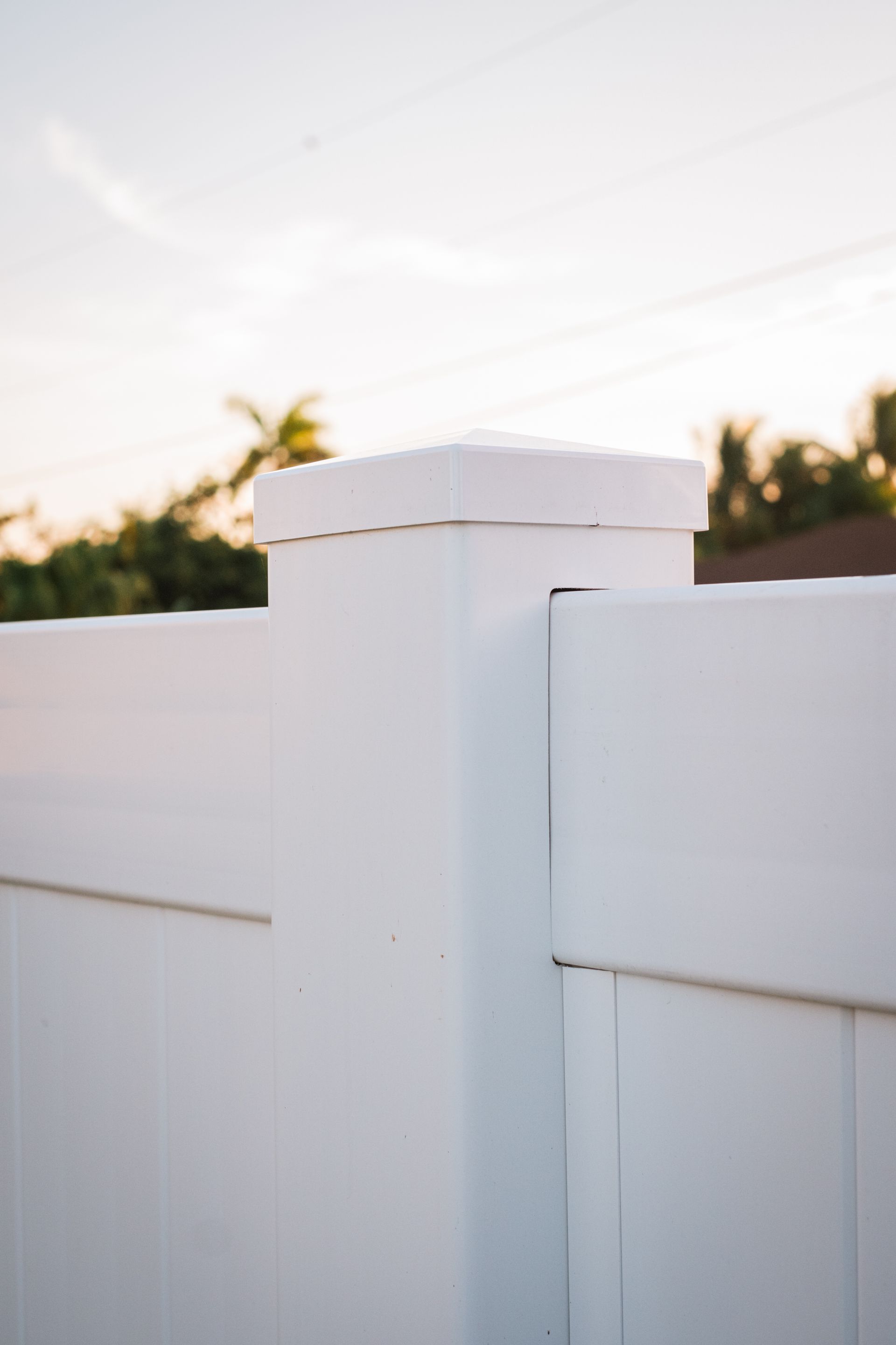 White vinyl fence and post with a square cap against a blurry sunset.