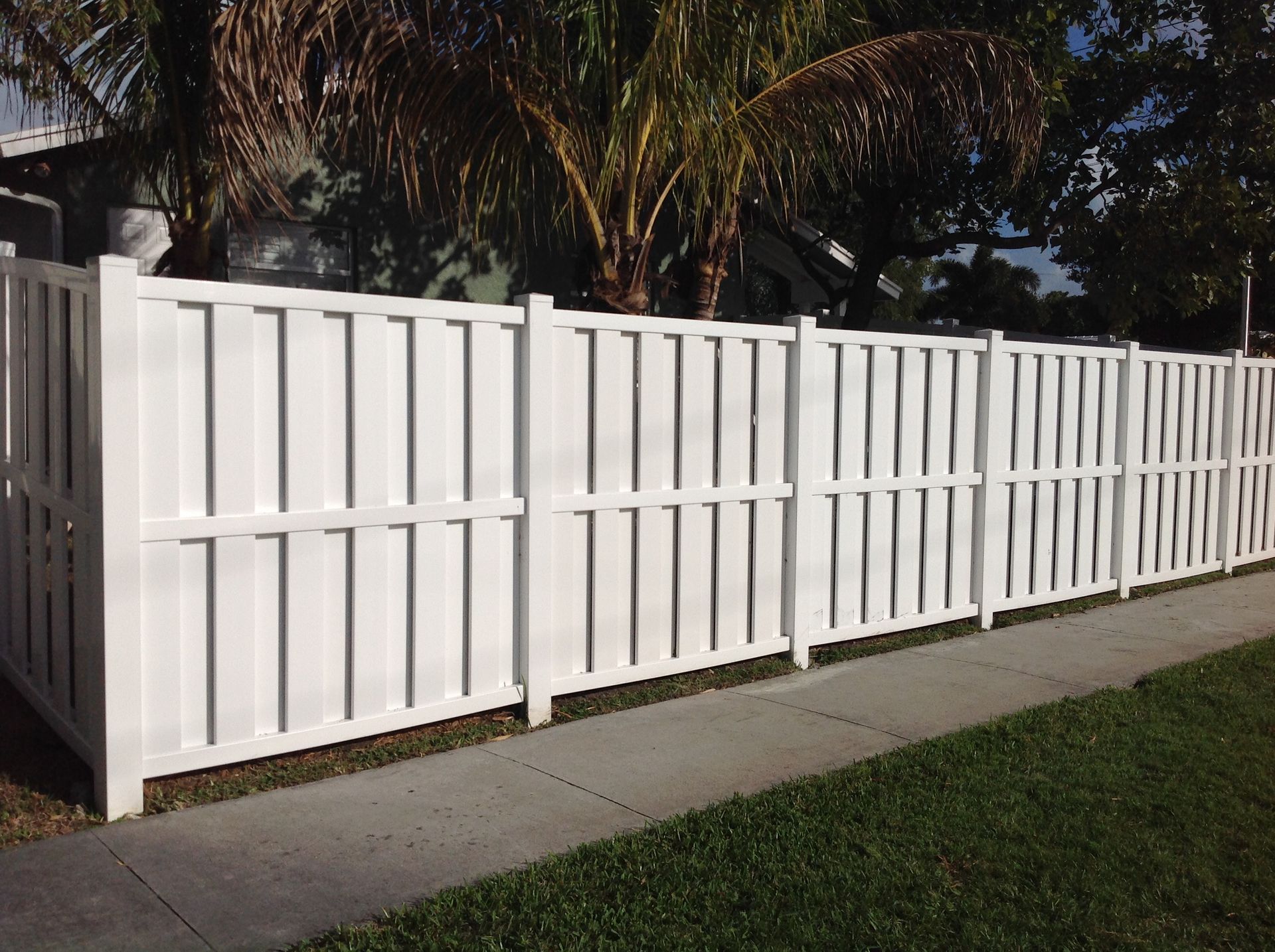 A white fence along a sidewalk in front of a house