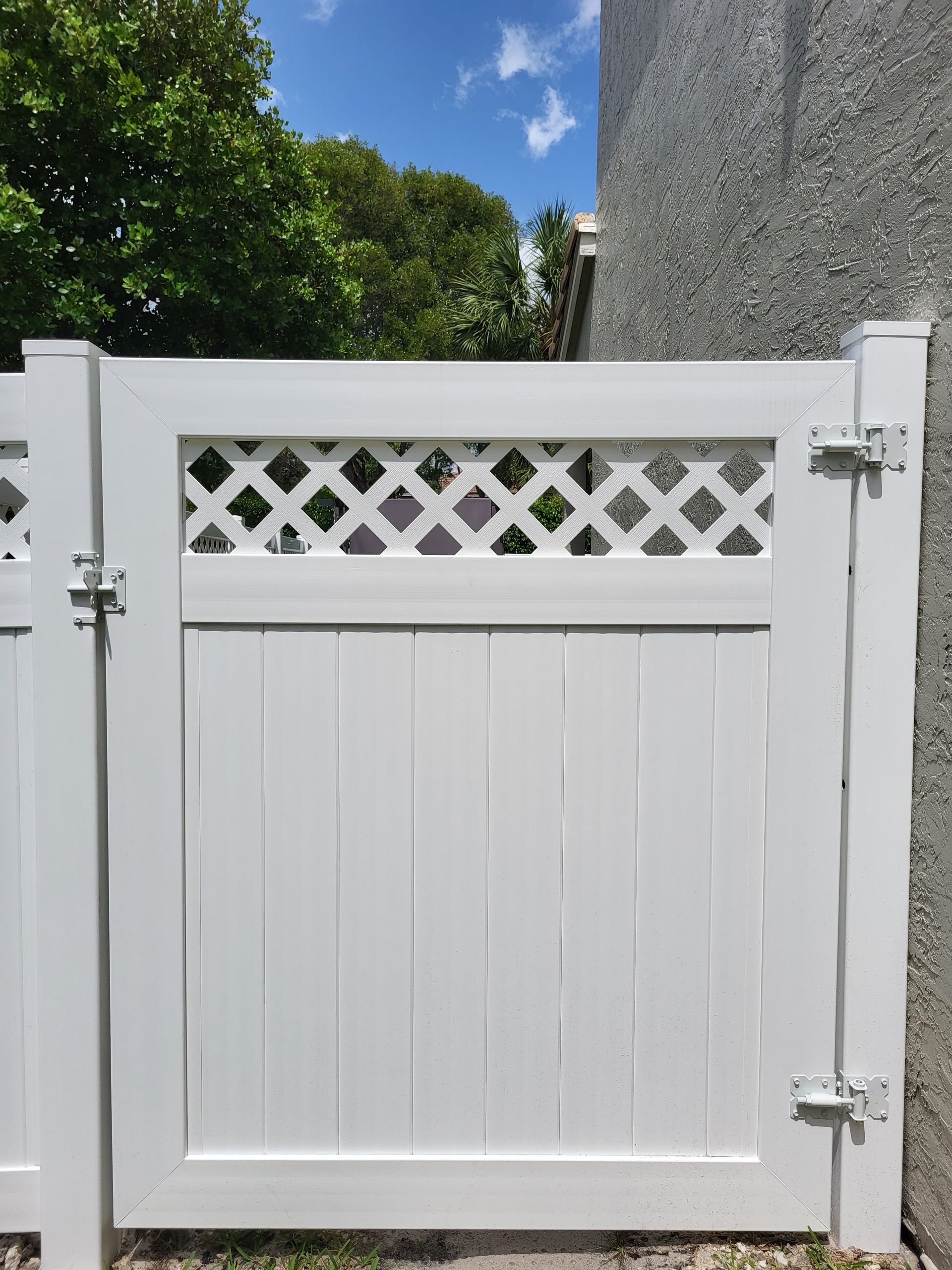 A white gate with a lattice design is sitting next to a concrete wall.