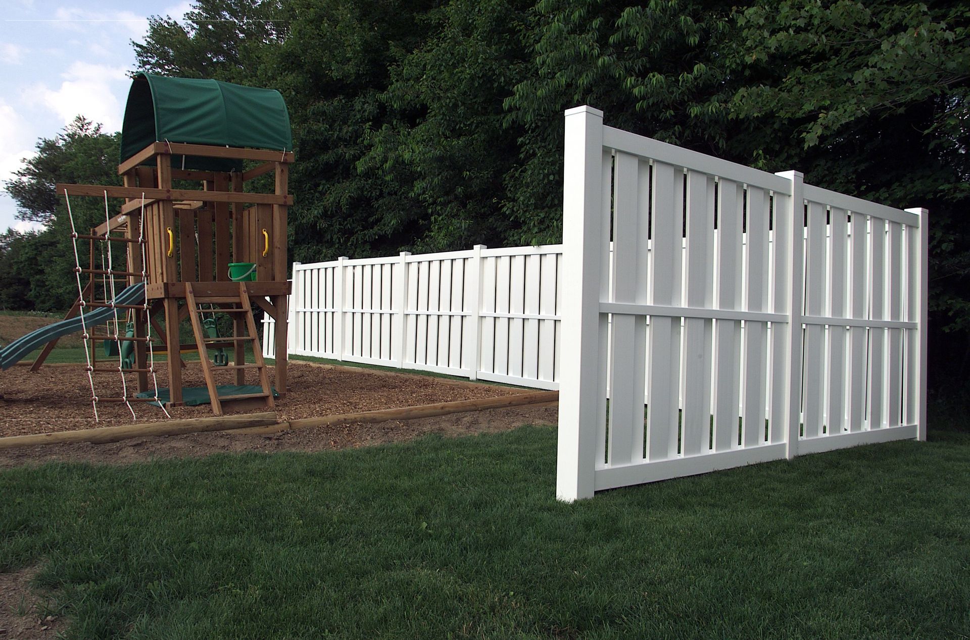 A white fence surrounds a playground with a swing set in the background