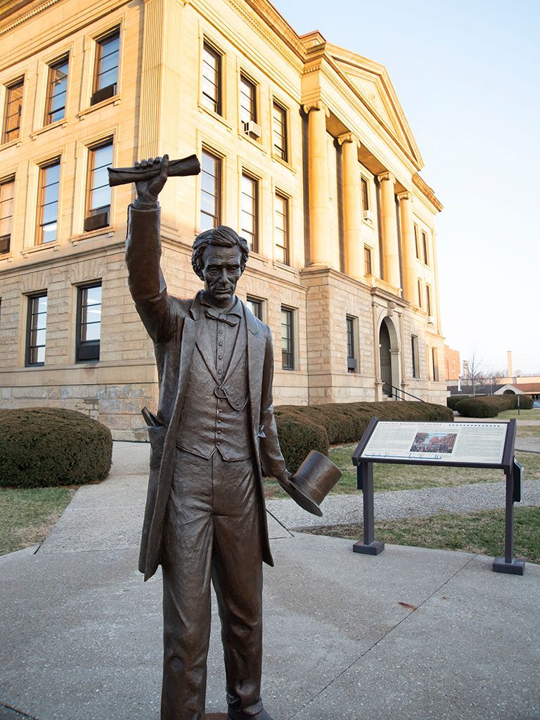 A statue of abraham lincoln holding a telescope and top hat in front of a large building.