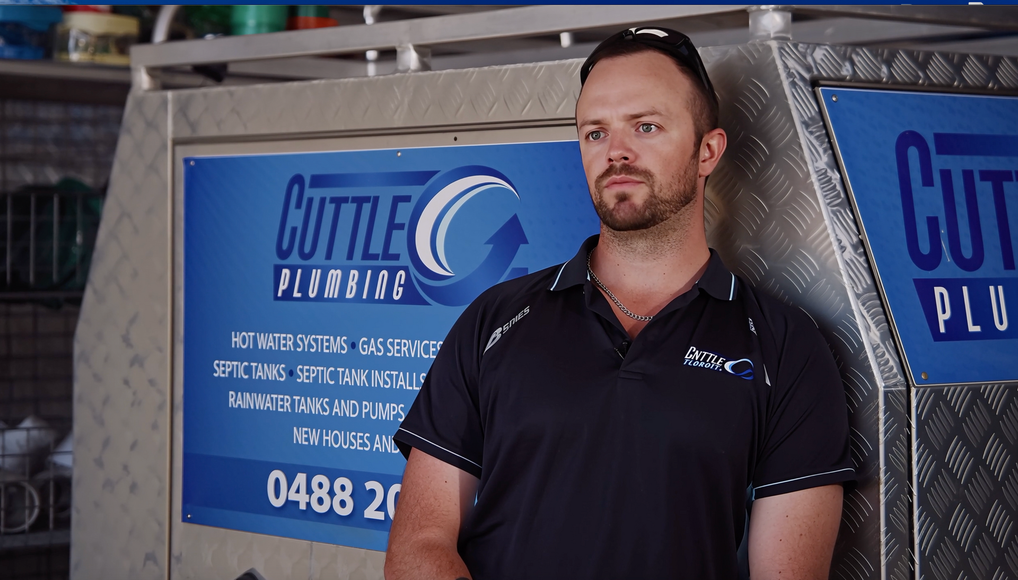 A person stands before a Cuttle Plumbing vehicle sign, leaning against its metallic exterior.