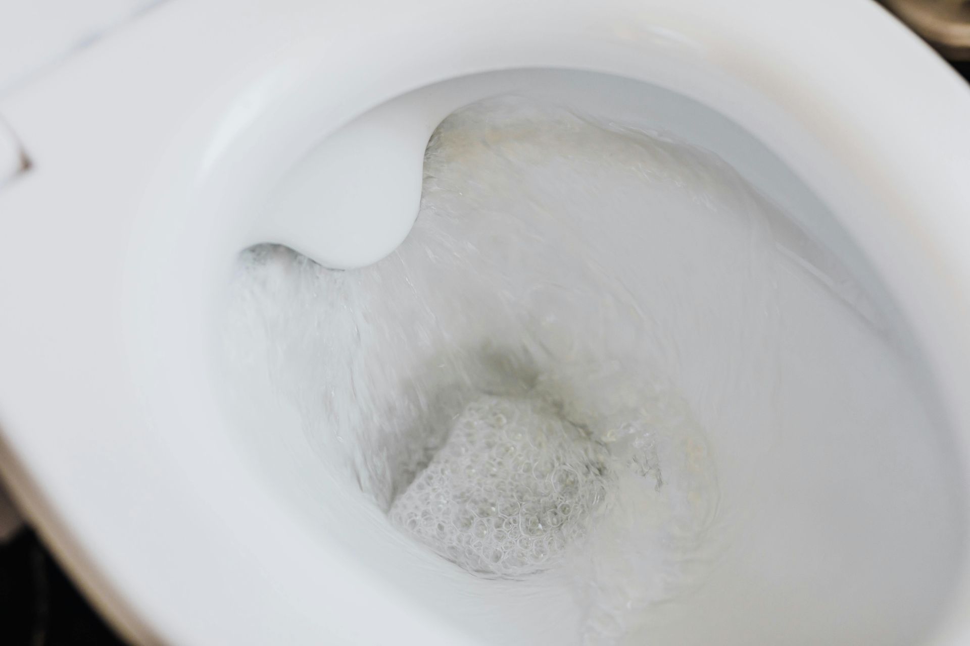 A close-up, high-angle view of a clean, white toilet bowl filled with clear, swirling water.