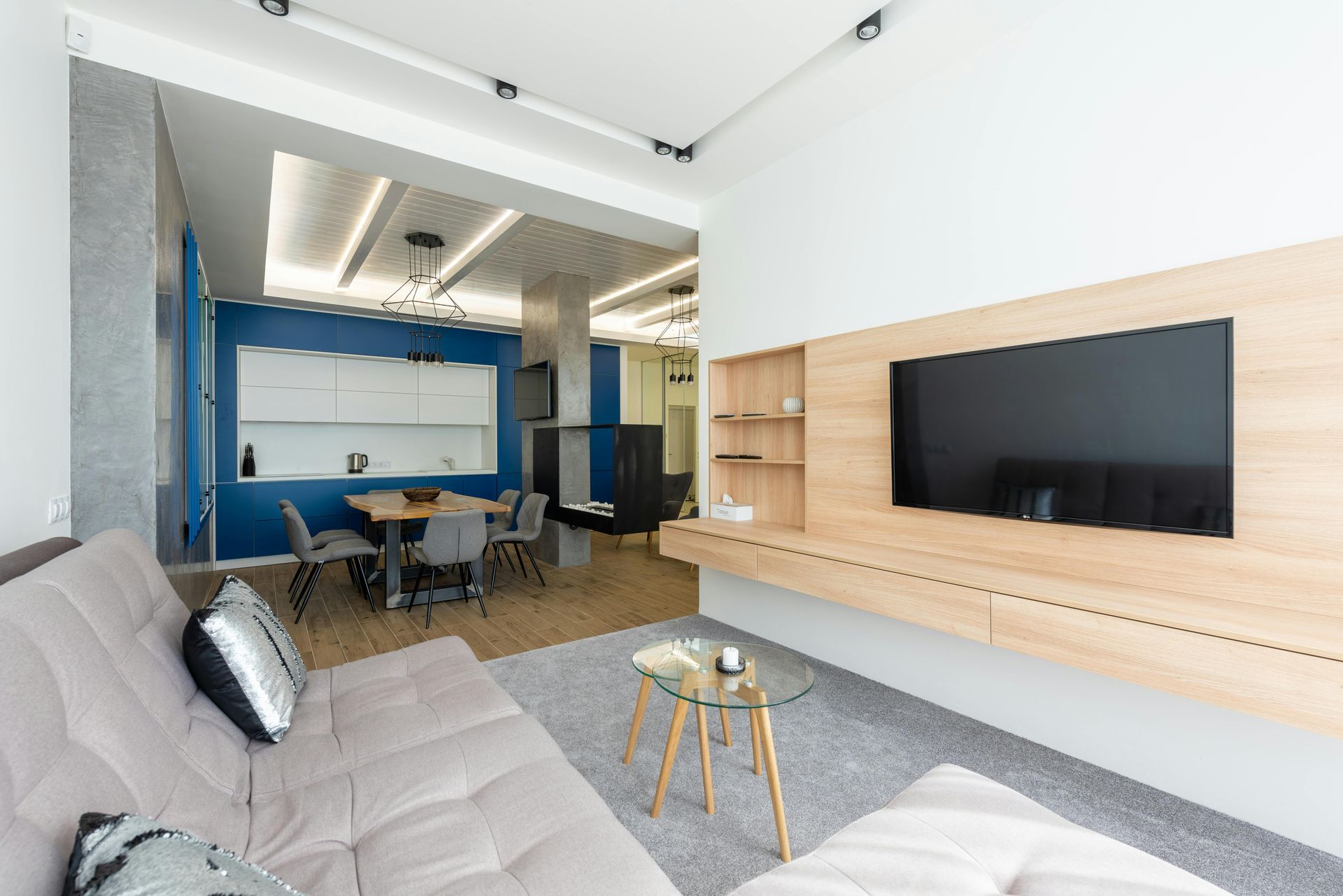 Modern living room with TV on wooden panel, sofa, and open kitchen area.