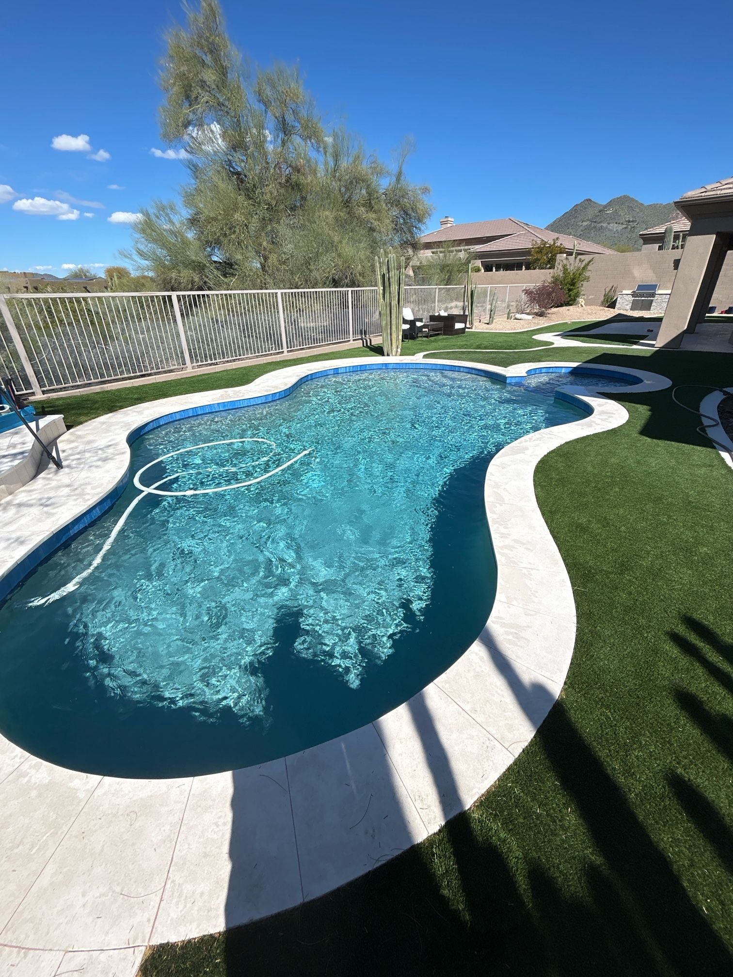 A large swimming pool surrounded by grass and a fence in a backyard.