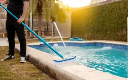 A man is cleaning a swimming pool with a mop.
