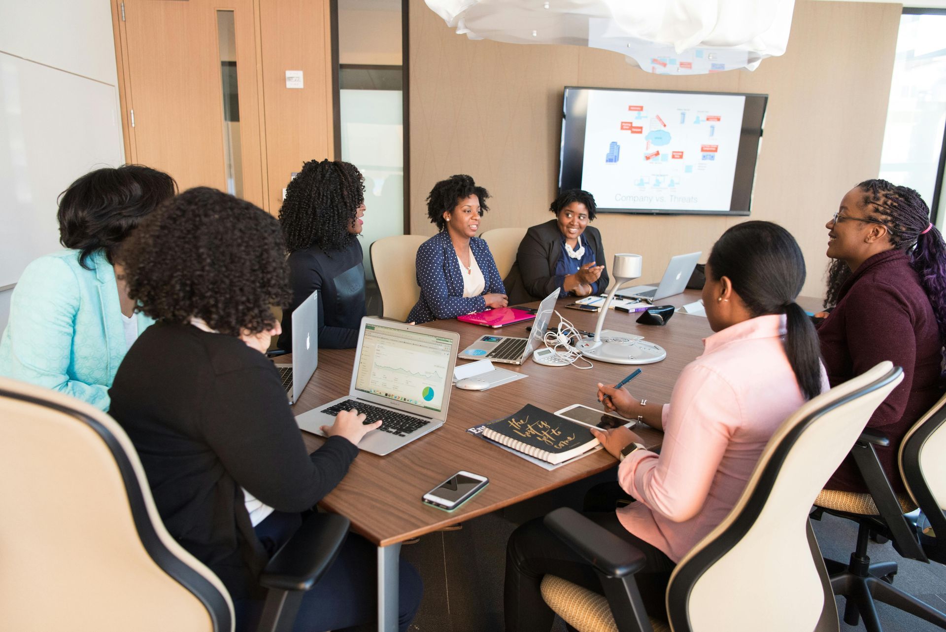 A group of women are sitting around a conference table with laptops.