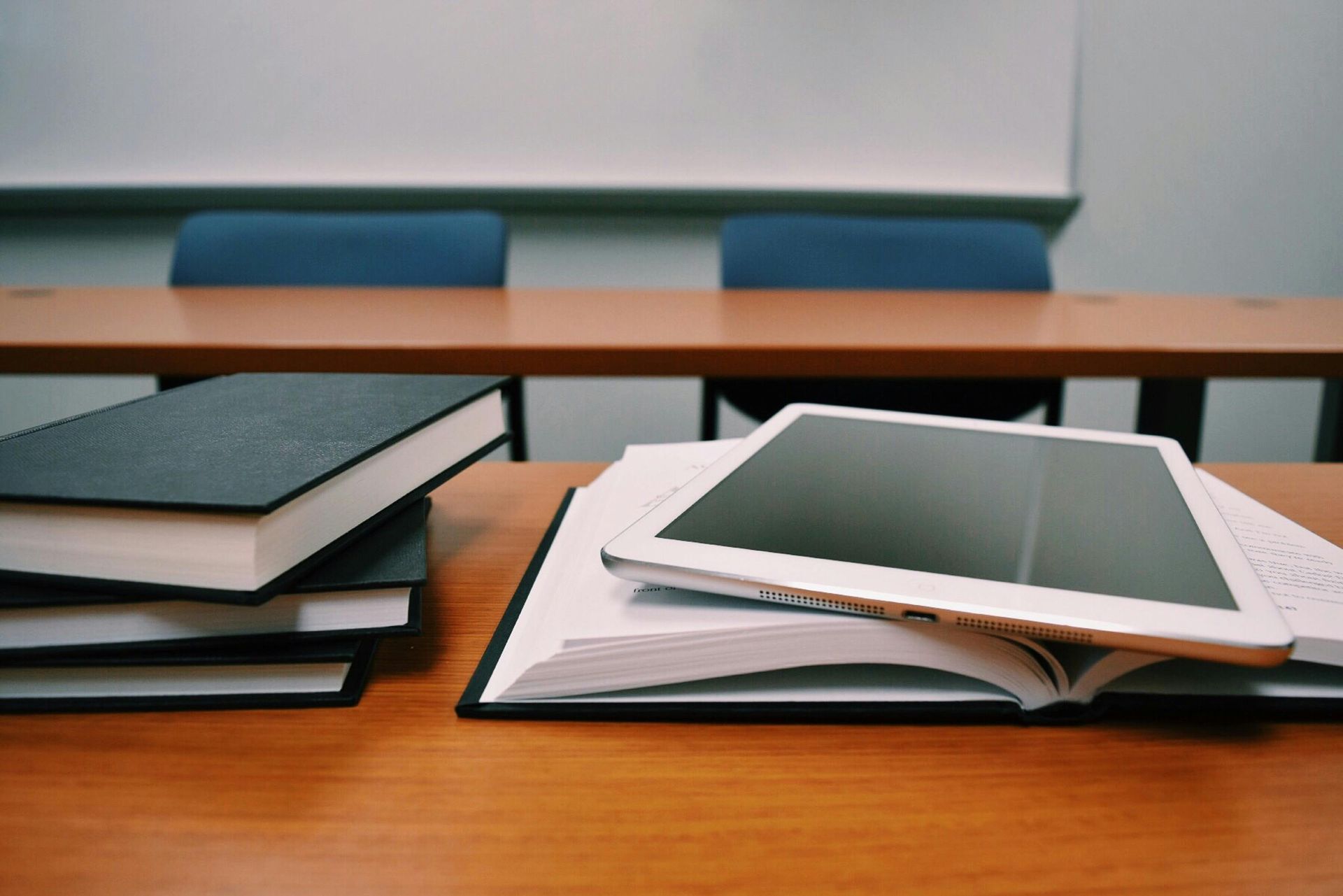 A stack of books and a tablet on a wooden table.