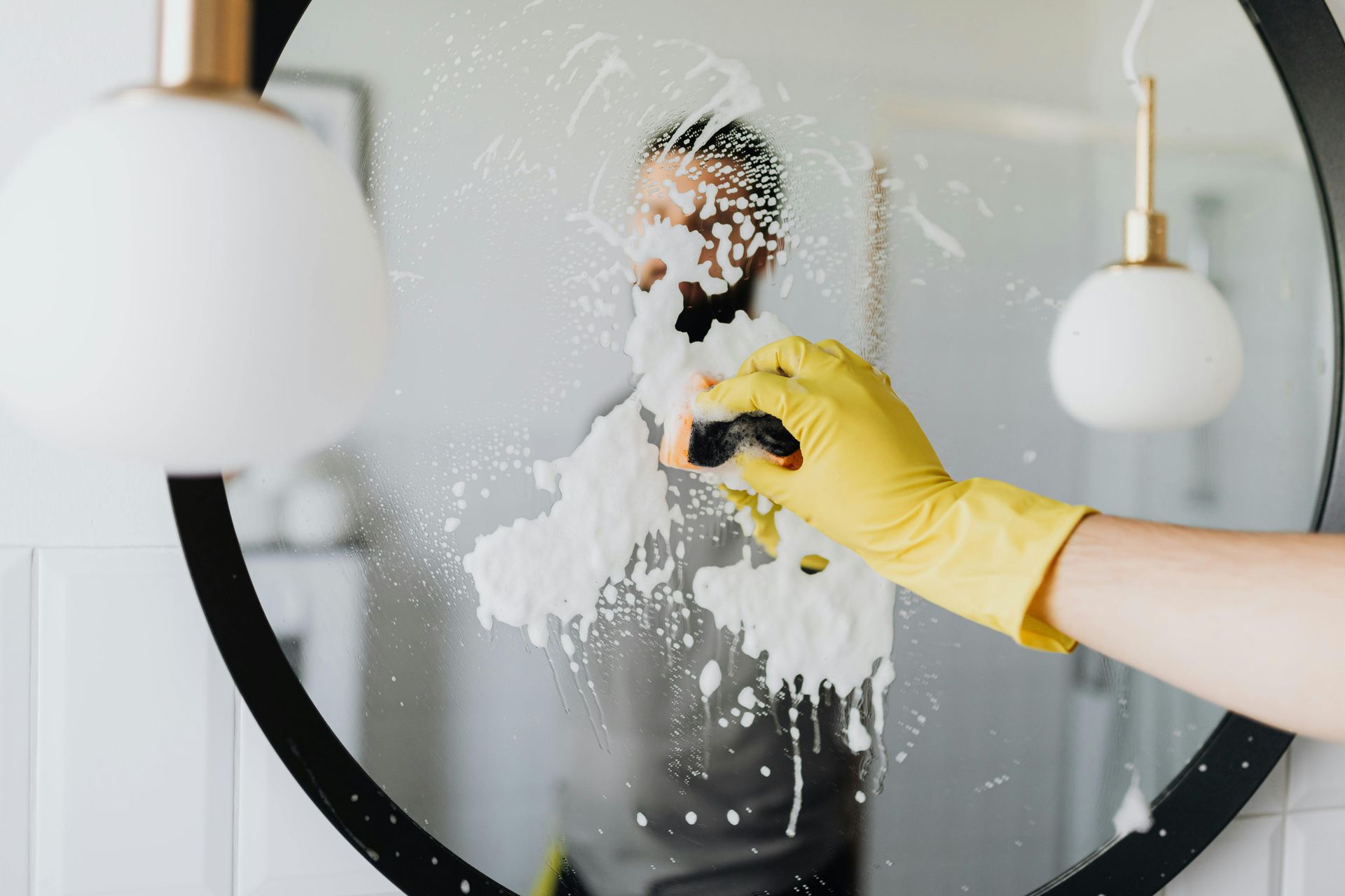 A person wearing yellow gloves is cleaning a mirror.